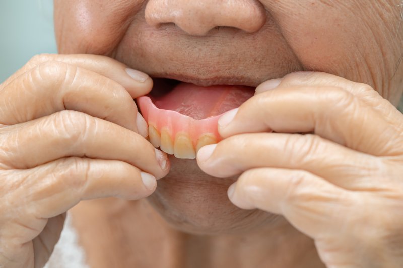 An older woman putting a denture in her mouth